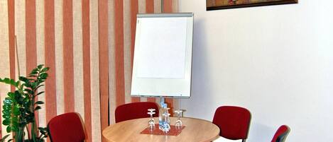 A conference room with a round table, red chairs, a whiteboard, a potted plant, and a painting on the wall.