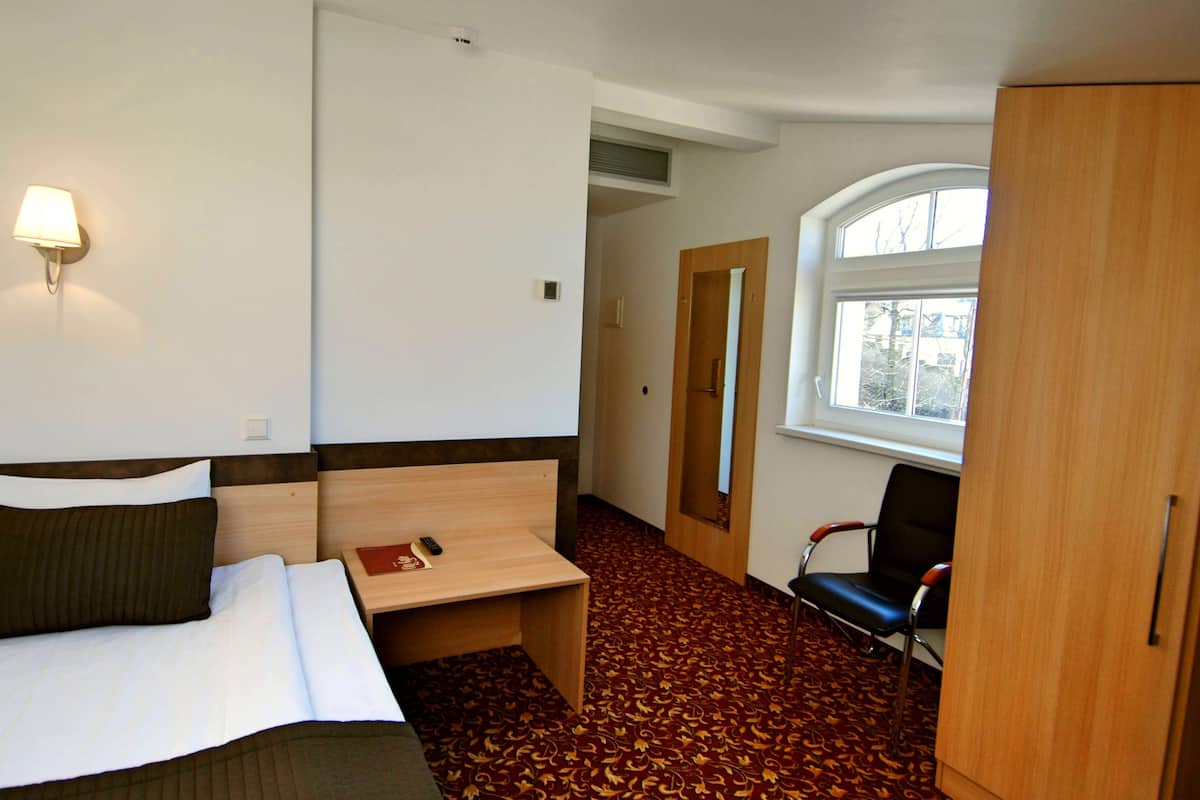 A hotel room with a bed, bedside table, lamp, chair, wardrobe, and a window.