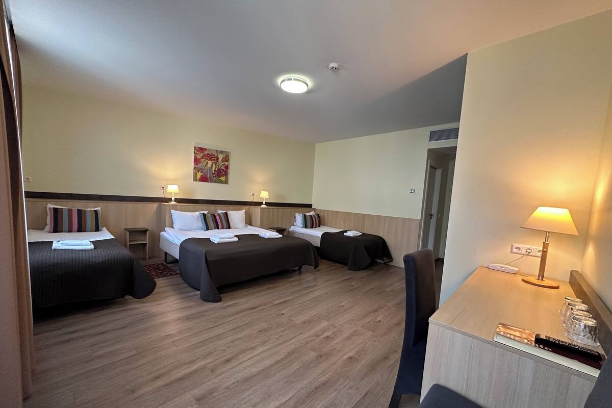 A hotel room with two beds, a desk, a chair, a lamp, and a painting on the wall.