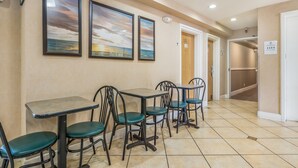 Un espace repas avec des tables et des chaises, des œuvres d’art encadrées accrochées au mur et un sol carrelé.