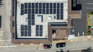 Vue aérienne d’un parking avec plusieurs rangées de voitures garées et des panneaux solaires sur le toit.