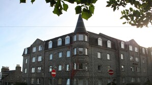 Un edificio de varios pisos con fachada de piedra, varias ventanas y una característica torreón en la esquina.