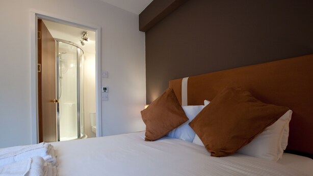 Una habitación de hotel con cama, almohadas, ducha y puerta.