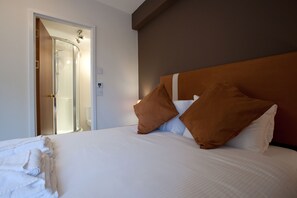 Una habitación de hotel con cama, almohadas, ducha y puerta.