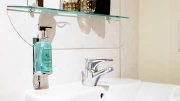 A bathroom with a white sink, a glass shelf above it, and a mirror reflecting a plant and bottles.