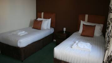 Two twin beds with brown headboards and white bedding, a small bedside table with a lamp, and a green carpet.