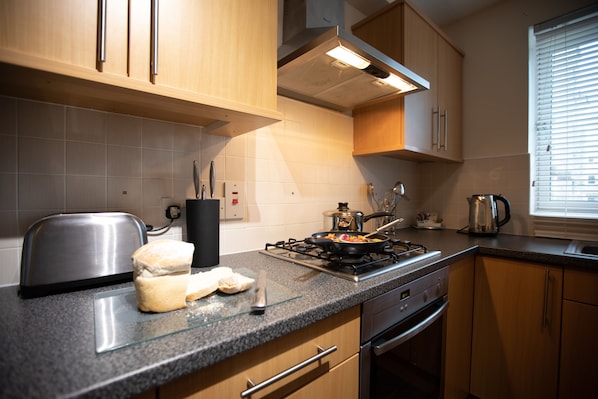 A modern kitchen with wooden cabinets, a gas stove, and a toaster. - The Spires Serviced Apartments Aberdeen (Aberdeen)
