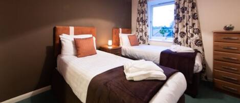 A hotel room with two beds, a dresser, and a window with curtains.