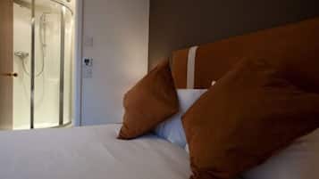A hotel room with a bed, brown pillows, and a glass shower enclosure.