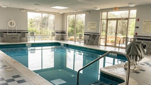 Piscina interior com paredes de vidro transparente, cadeira de salva-vidas e aviso indicando que não há salva-vidas de serviço.