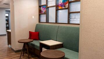 A green sofa with a red pillow, two wooden side tables, and a colorful abstract art piece on the wall.