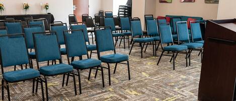 A conference room with rows of blue chairs, a podium, and a carpeted floor.