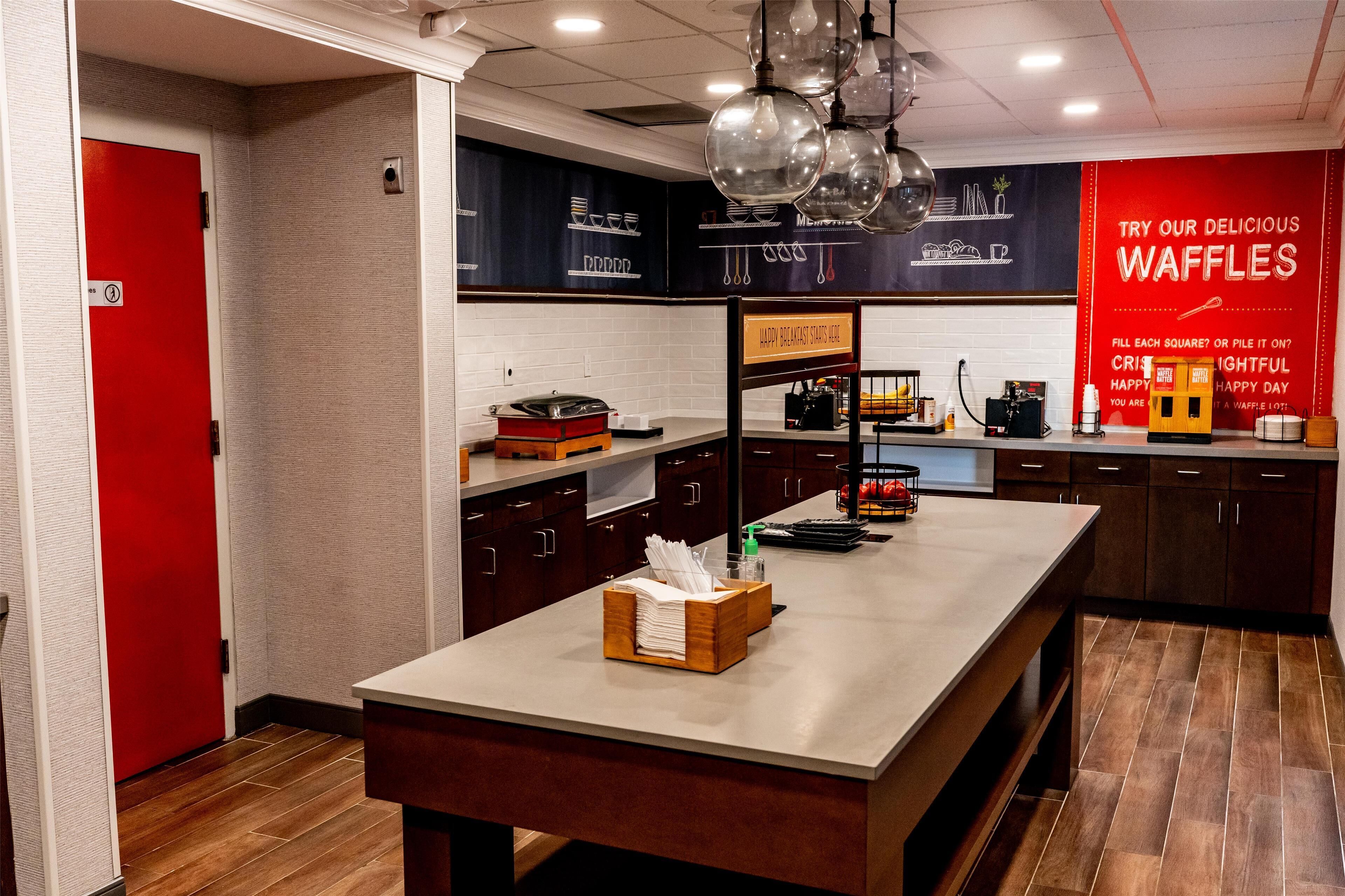 A modern kitchen area with a central island, a red door, and a waffle advertisement on the wall.