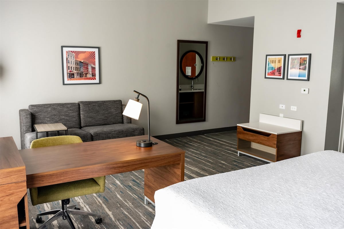 A hotel room with a bed, a desk, a chair, a sofa, a small table, a mirror, and two framed pictures on the wall.