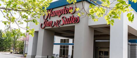 Hampton Inn & Suites -hotellin ulkoasu: siinä on suuri kyltti, koristeelliset pylväät ja katettu sisäänkäyntialue.