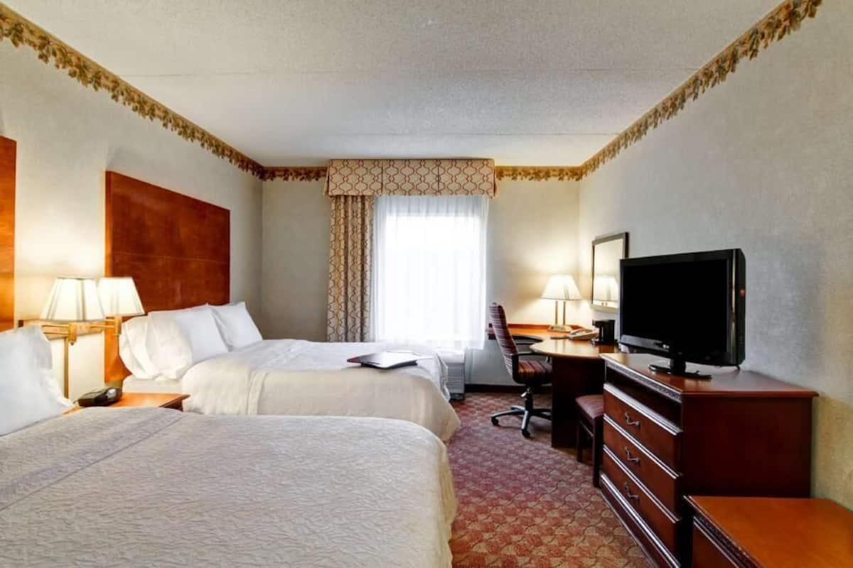 A hotel room with two beds, a desk with a chair, a television, and a dresser.