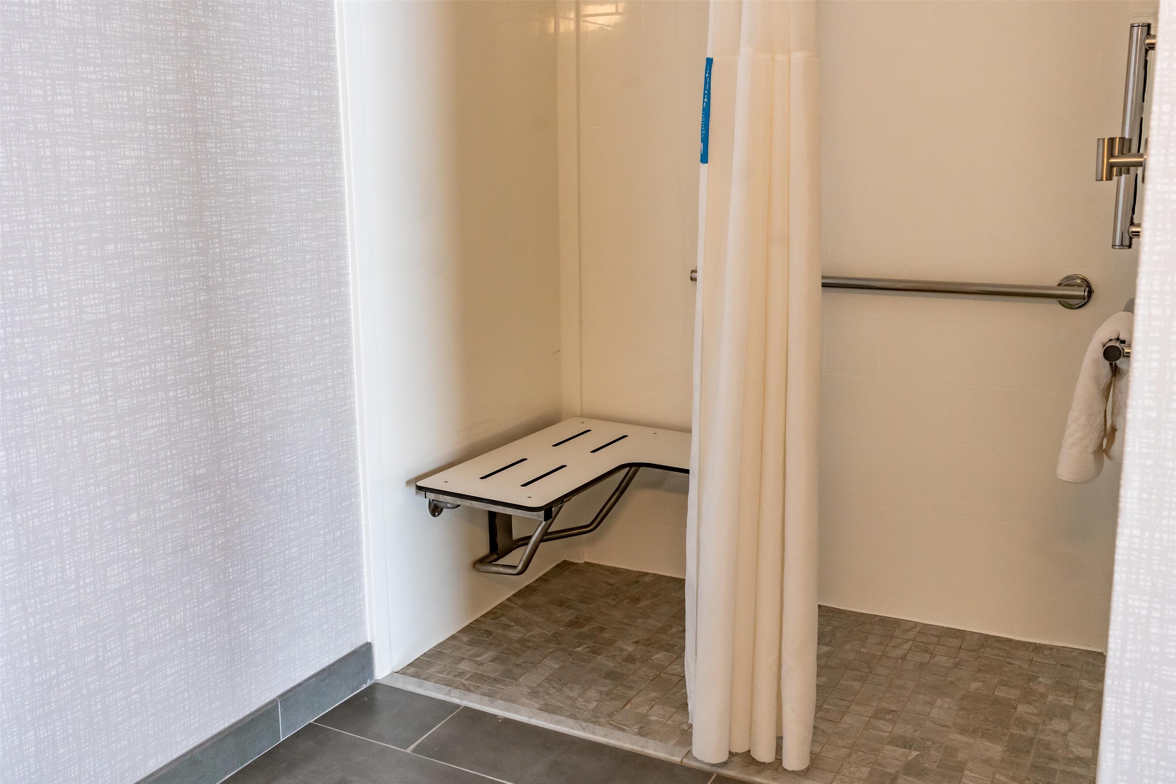A small, enclosed shower area with a bench, a towel rack, and a grab bar.