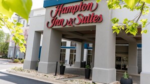 Exterior do Hampton Inn & Suites, com entrada desobstruída, pilares grandes e uma placa de sinalização.