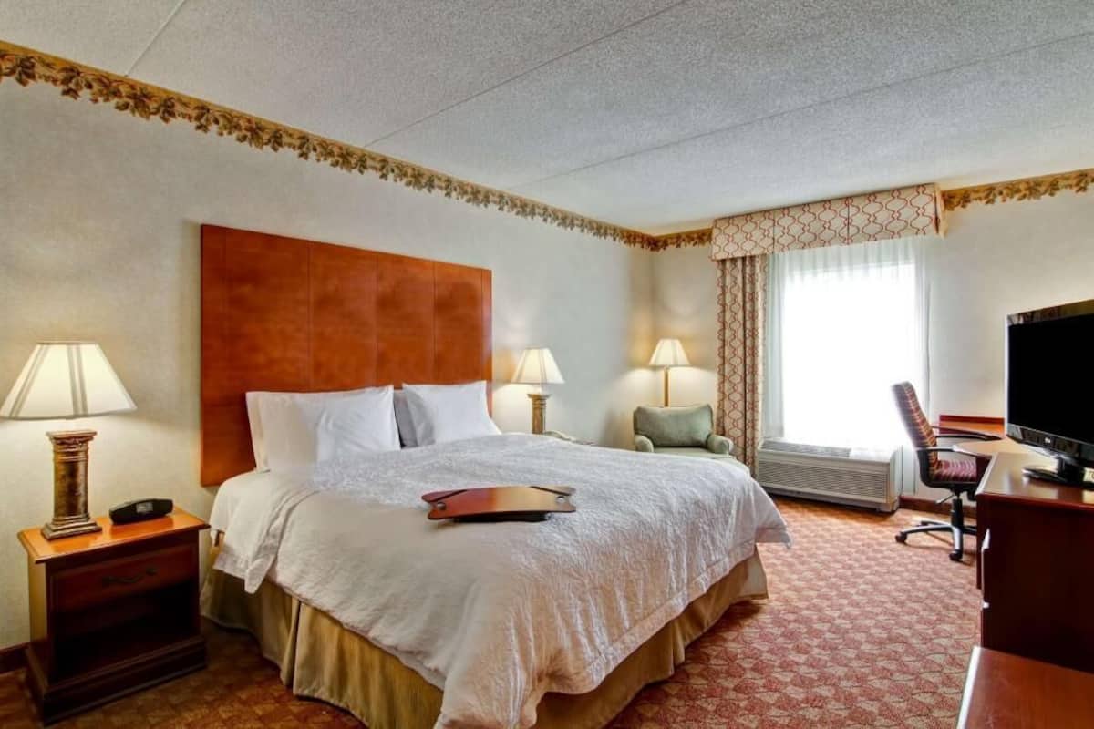 A hotel room with a large bed, two bedside lamps, a desk with a television, and a window with curtains.