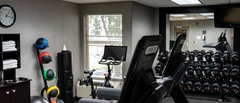A gym with exercise equipment, a clock, and a window with blinds.