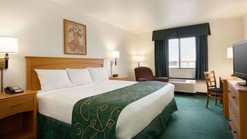 A hotel room with a large bed, two bedside tables with lamps, a desk with a chair, a television, and a window with curtains.