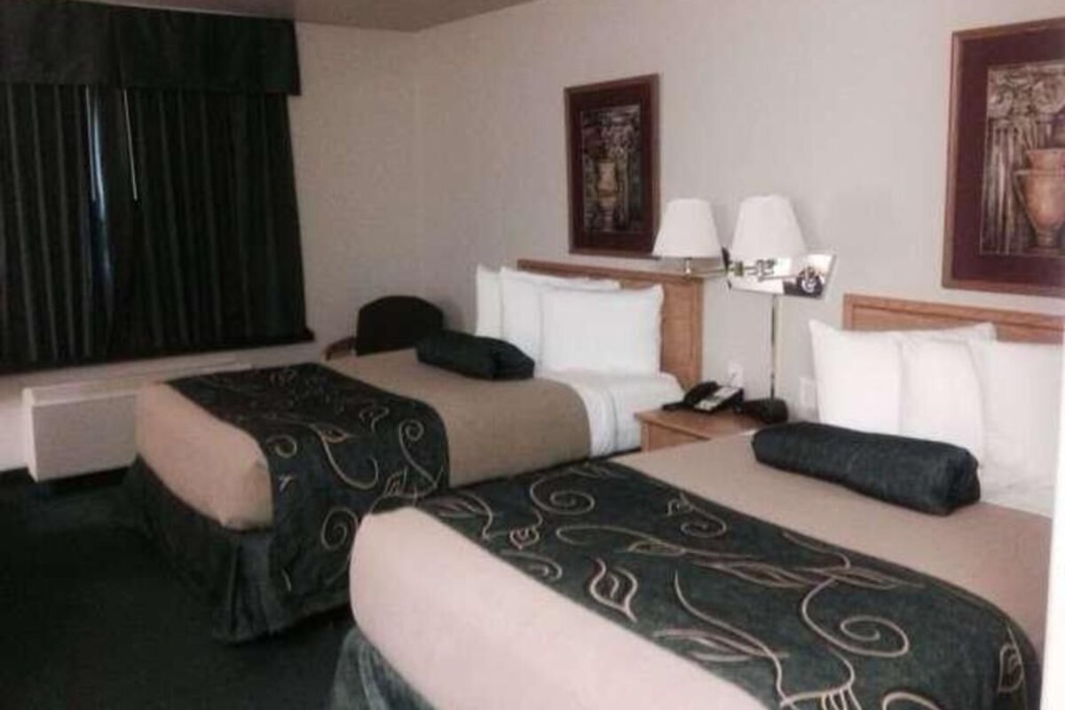 Une chambre d’hôtel avec deux lits, un bureau, une chaise, une lampe et des œuvres d’art accrochées aux murs.