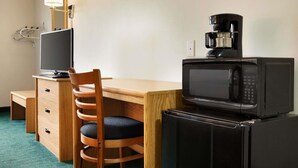 A compact hotel room with a wooden desk, a chair, a television, a microwave, and a coffee maker. - Travelodge by Wyndham Milford (Milford)