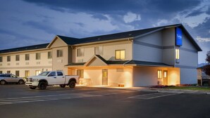 A hotel with a modern design, featuring a parking lot with a white pickup truck and a compact car. - Travelodge by Wyndham Milford (Milford)