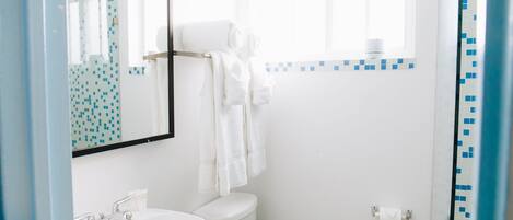 Un baño con lavamanos blanco, inodoro y ventana sobre el inodoro.