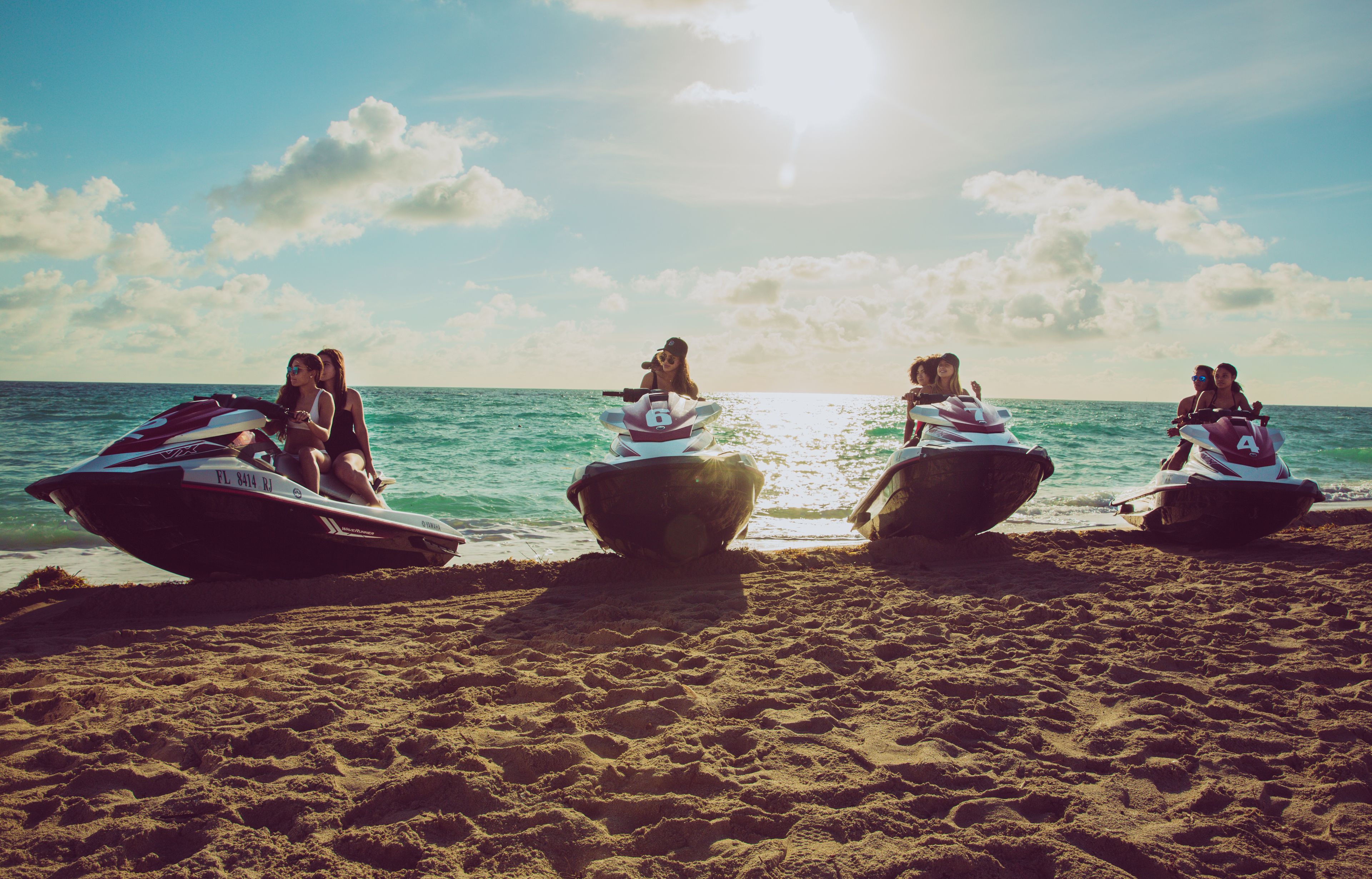 Un grupo de motos acuáticas en una playa arenosa con el océano al fondo.