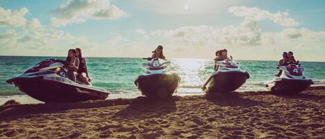 A group of jet skis on a sandy beach with the ocean in the background.