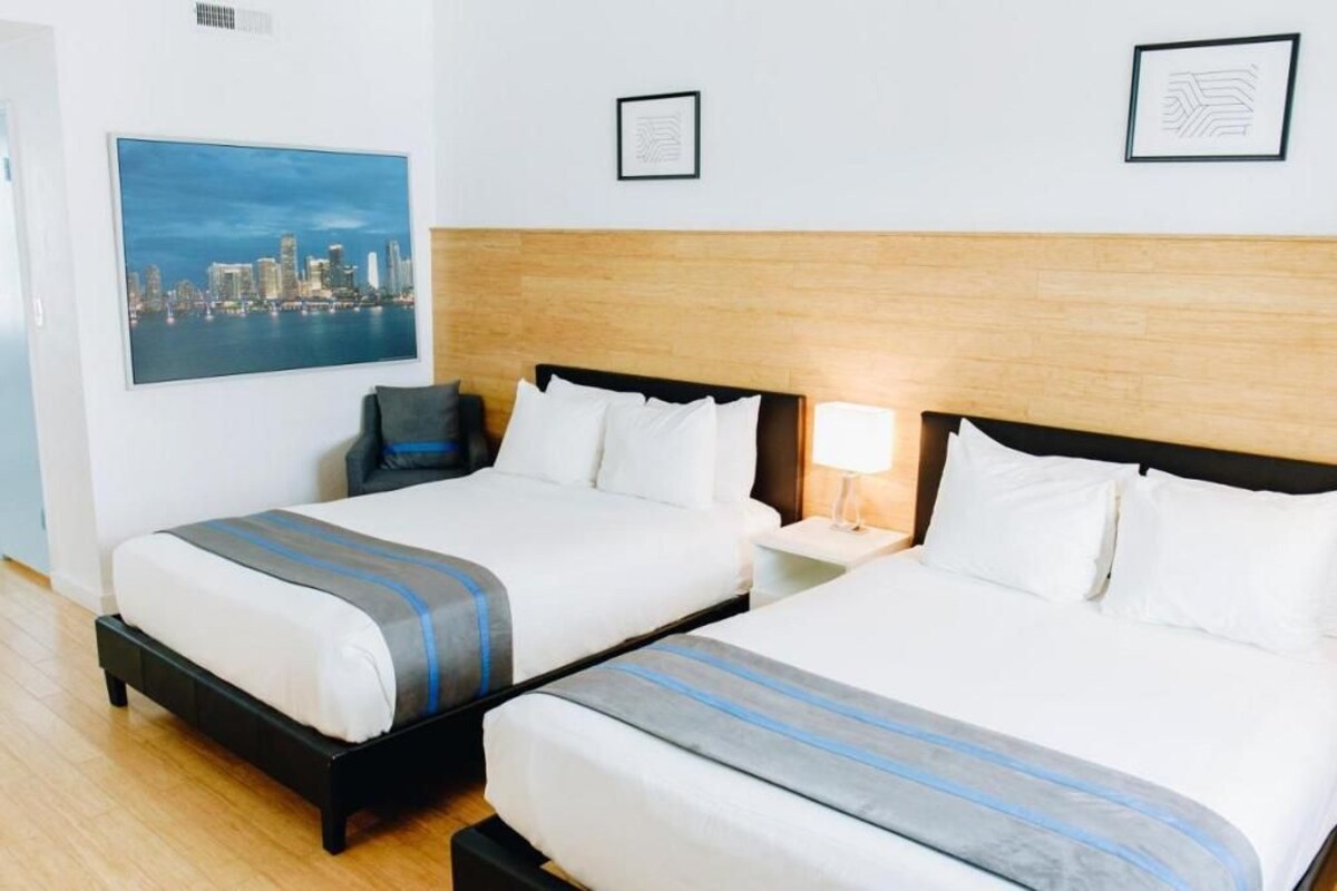 A hotel room with two beds, a cityscape painting, and framed artwork on the walls.
