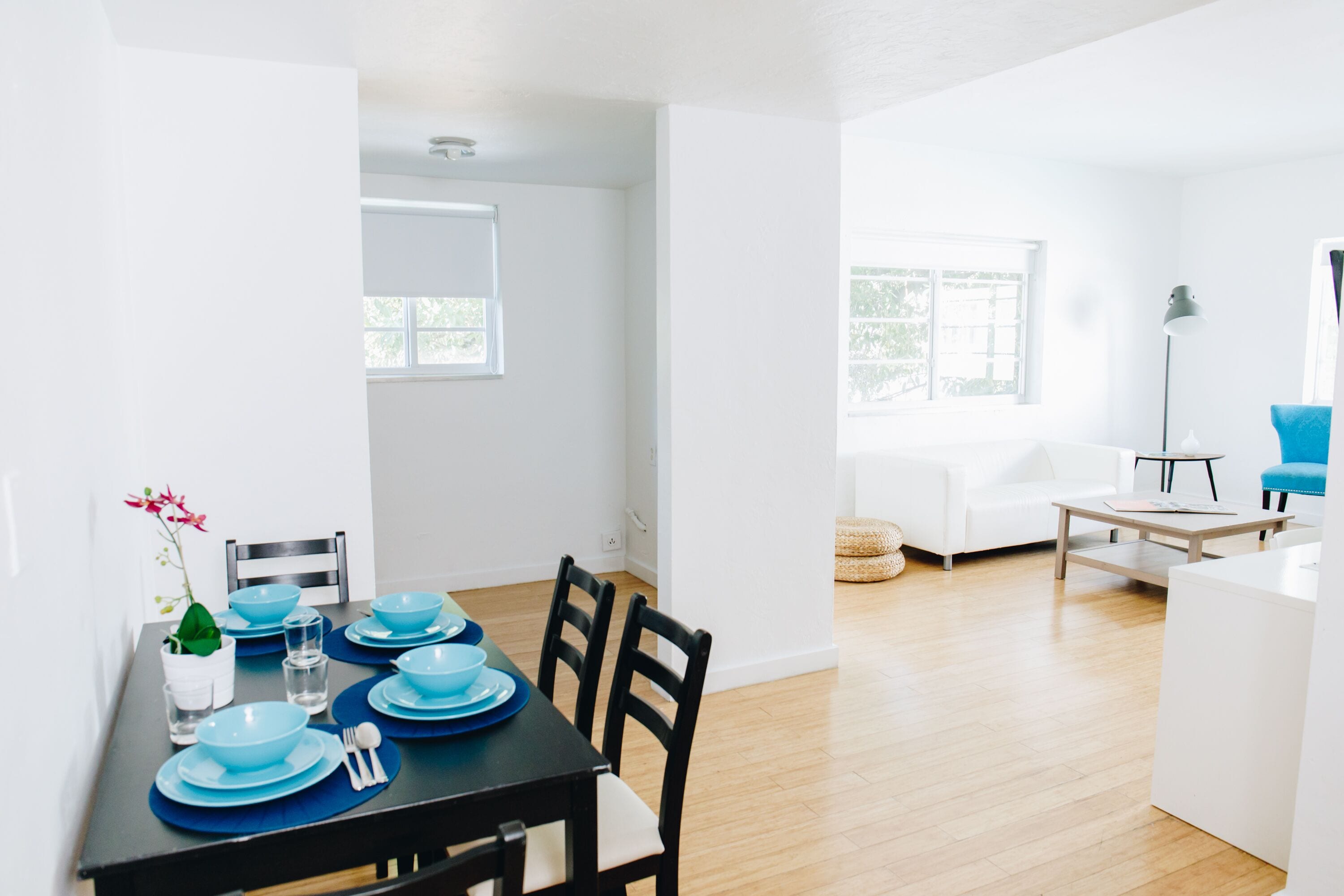 A modern dining area with a black table set for four, white walls, and a wooden floor.
