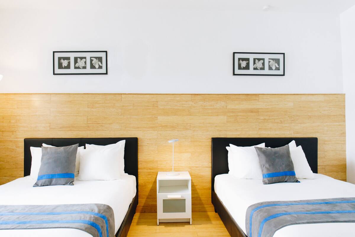 A hotel room with two beds, a wooden headboard, a nightstand, and framed pictures on the wall.