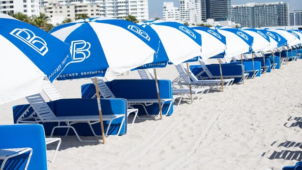 A row of beach umbrellas and lounge chairs with the logo 'Boucher Brothers' on them. - Aqua Hotel & Suites (Miami Beach)