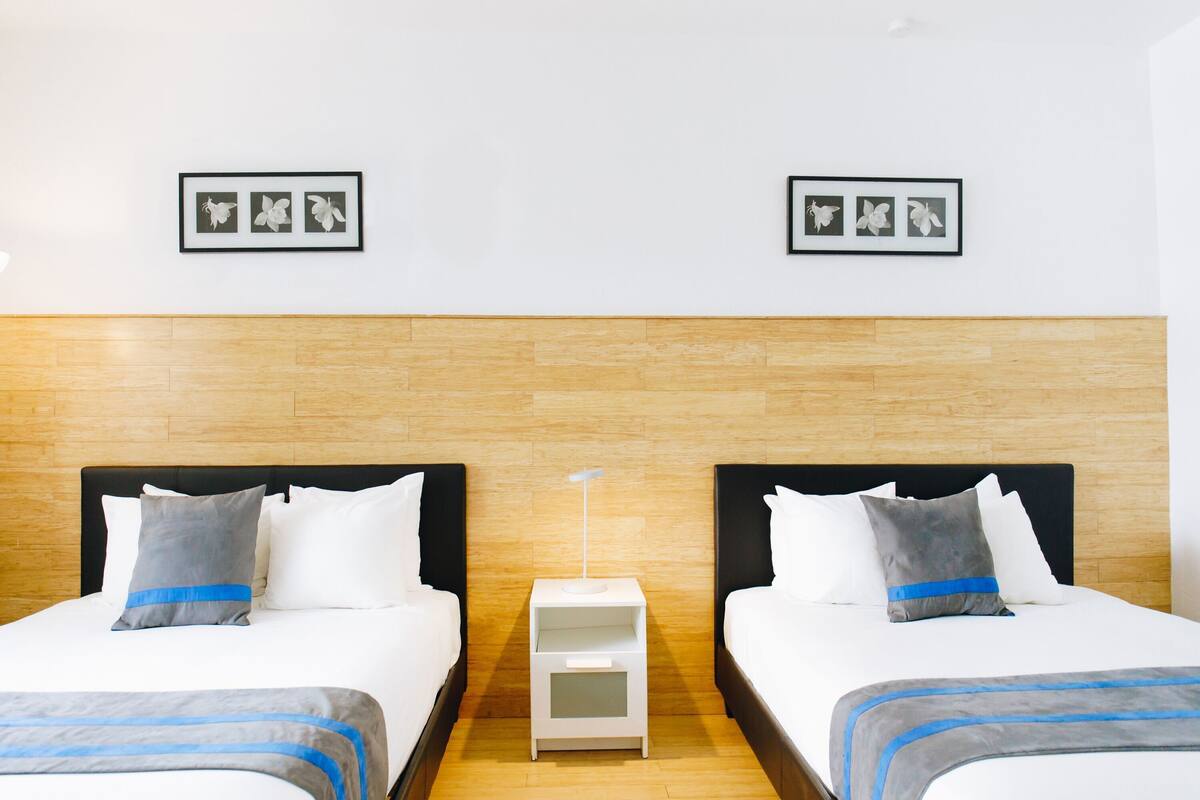 A hotel room with two beds, a nightstand, and framed pictures on the wall.