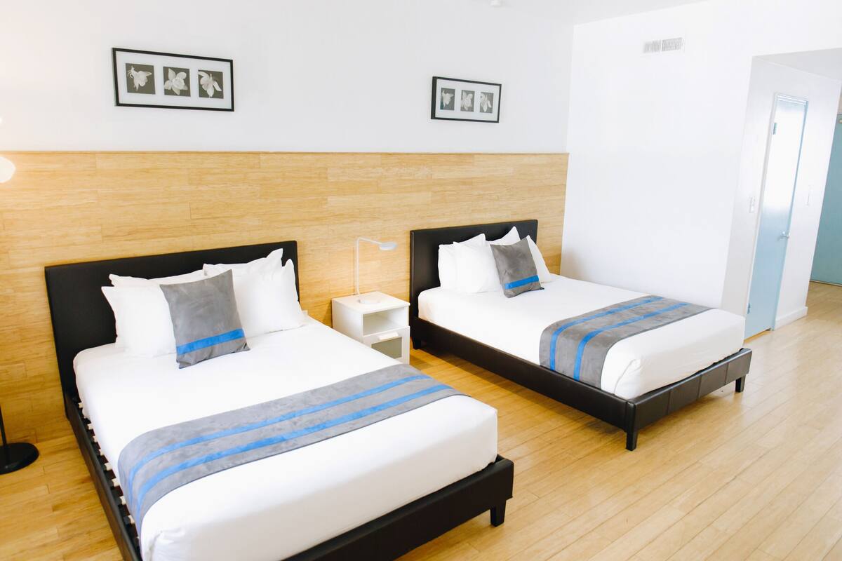 A hotel room with two beds, wooden flooring, and a white door.