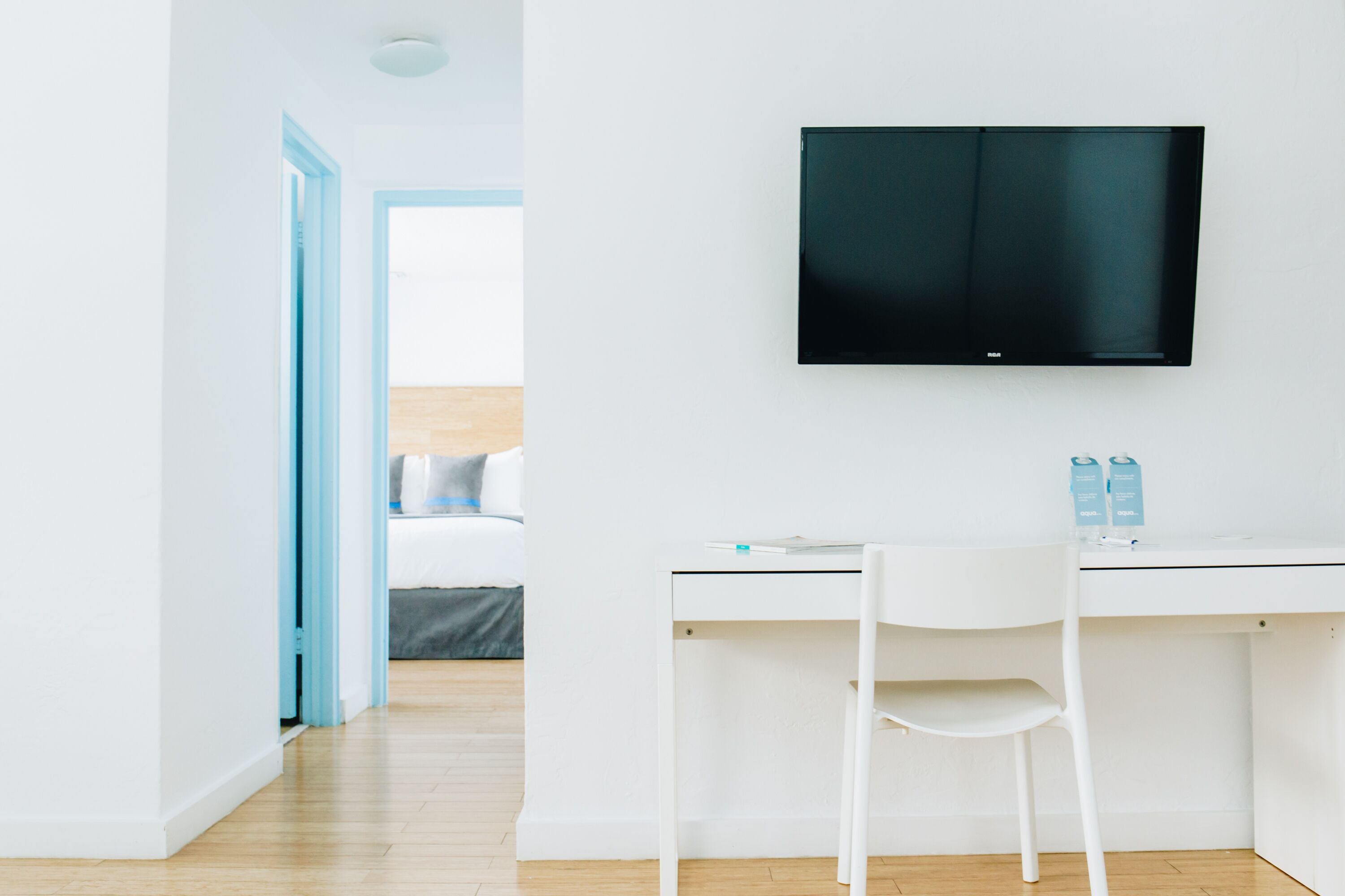 Una habitación moderna con un escritorio blanco, una silla blanca y un televisor de pantalla plana montado en la pared.