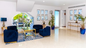 A modern living room with a glass coffee table, two blue armchairs, a blue rug, and a view of a tropical garden through a large window. - Aqua Hotel & Suites (Miami Beach)