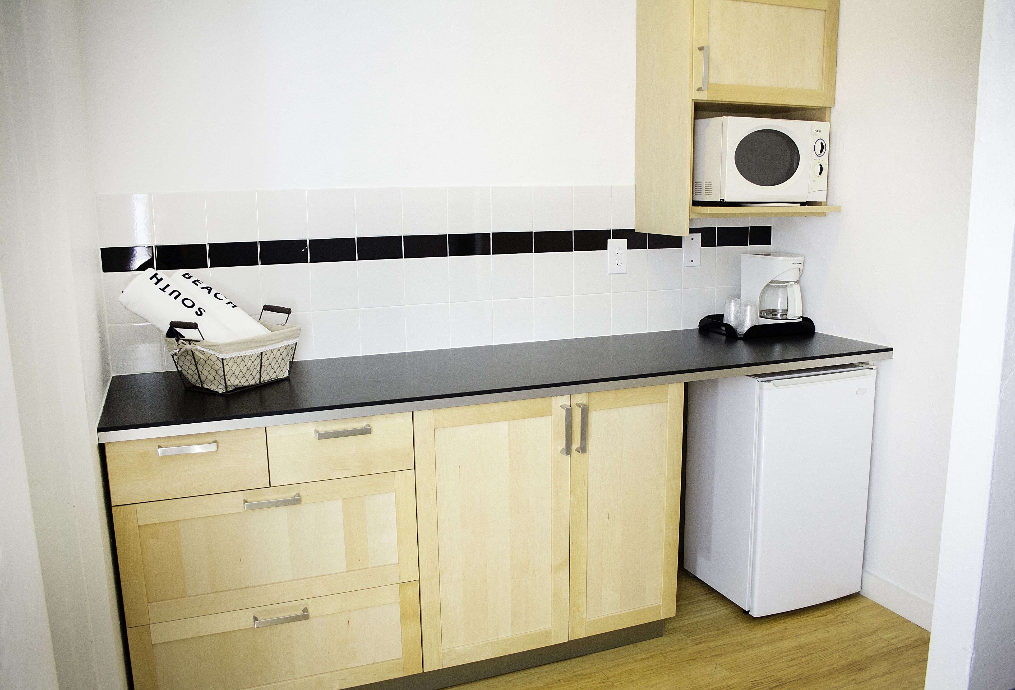 Una cucina compatta con mobili in legno, un piano di lavoro nero, un forno a microonde, una macchina da caffè e un piccolo frigorifero.