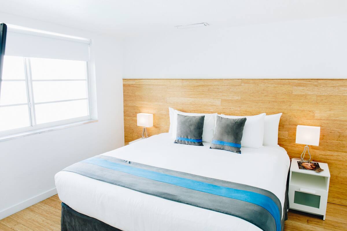 A hotel room with a large bed, wooden headboard, two bedside tables with lamps, and a window with curtains.