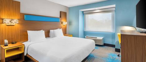 A hotel room with a bed, bedside tables, a desk, a chair, a window, and a wall-mounted air conditioning unit.