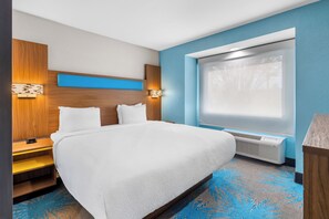 A hotel room with a large bed, a nightstand, a wall-mounted lamp, a window with a view, and a built-in air conditioning unit. - Days Inn & Suites by Wyndham Brandon Amphitheater (Brandon)