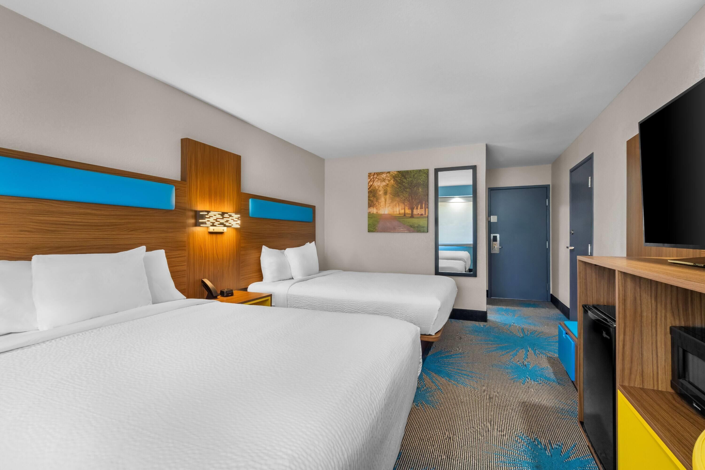 A hotel room with two beds, a TV, a desk, and a bathroom door.