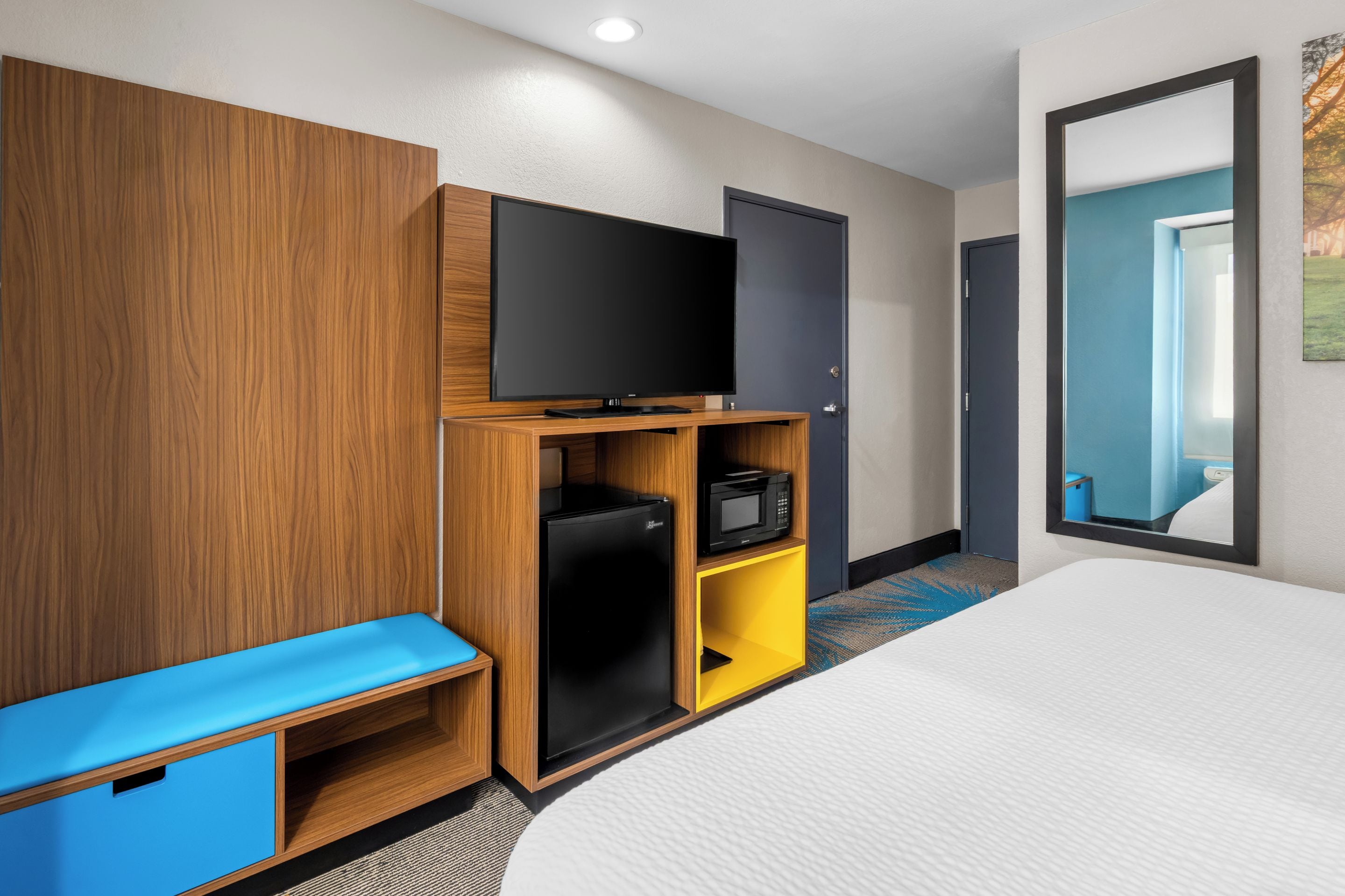 A hotel room with a bed, a television, a minibar, and a wardrobe.