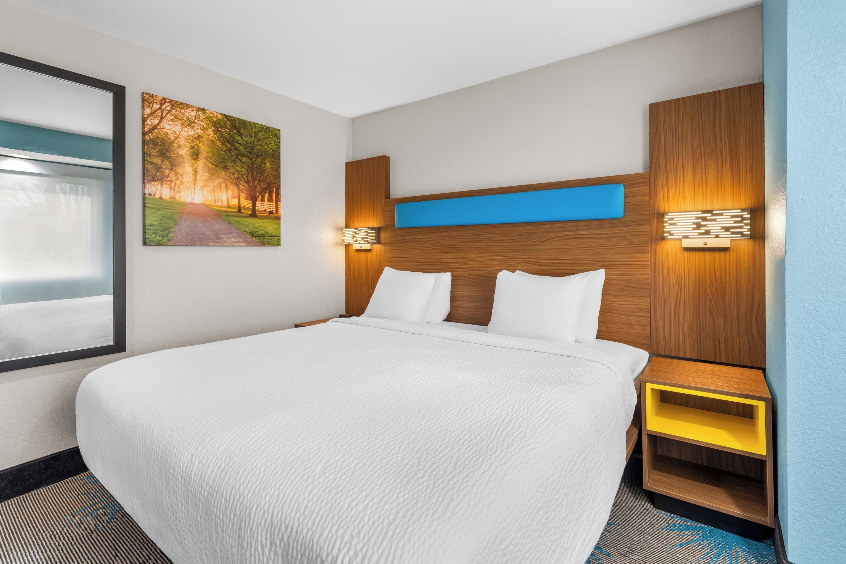 Een hotelkamer met een groot bed, een nachtkastje, een wandlamp en een lijst met een afbeelding.