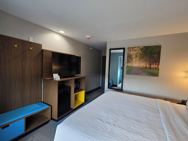 A hotel room with a large bed, a TV on a wooden stand, a small desk, and a mirror on the wall.