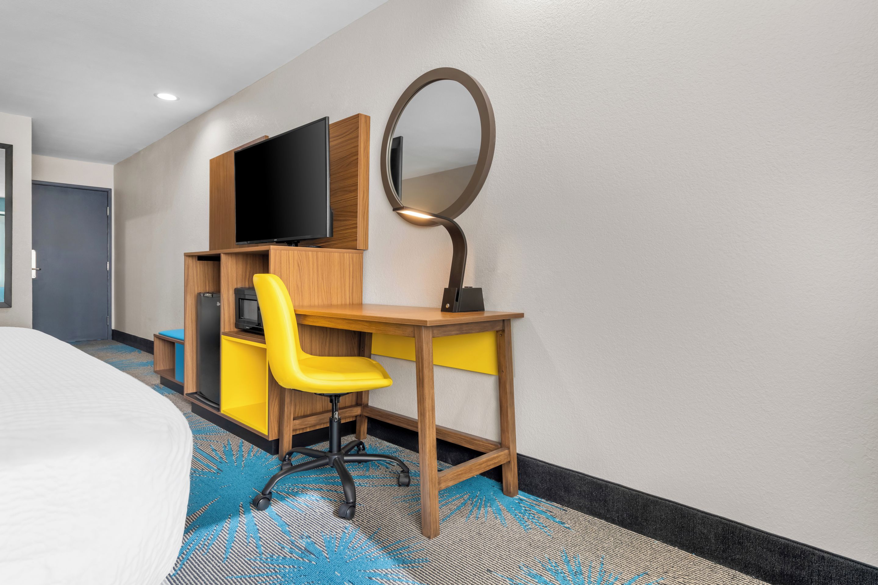 Una habitación de hotel con una cama, un escritorio, una silla, un televisor y un espejo.