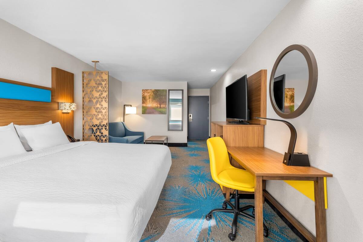 A hotel room with a bed, a desk with a chair, a TV, and a mirror.