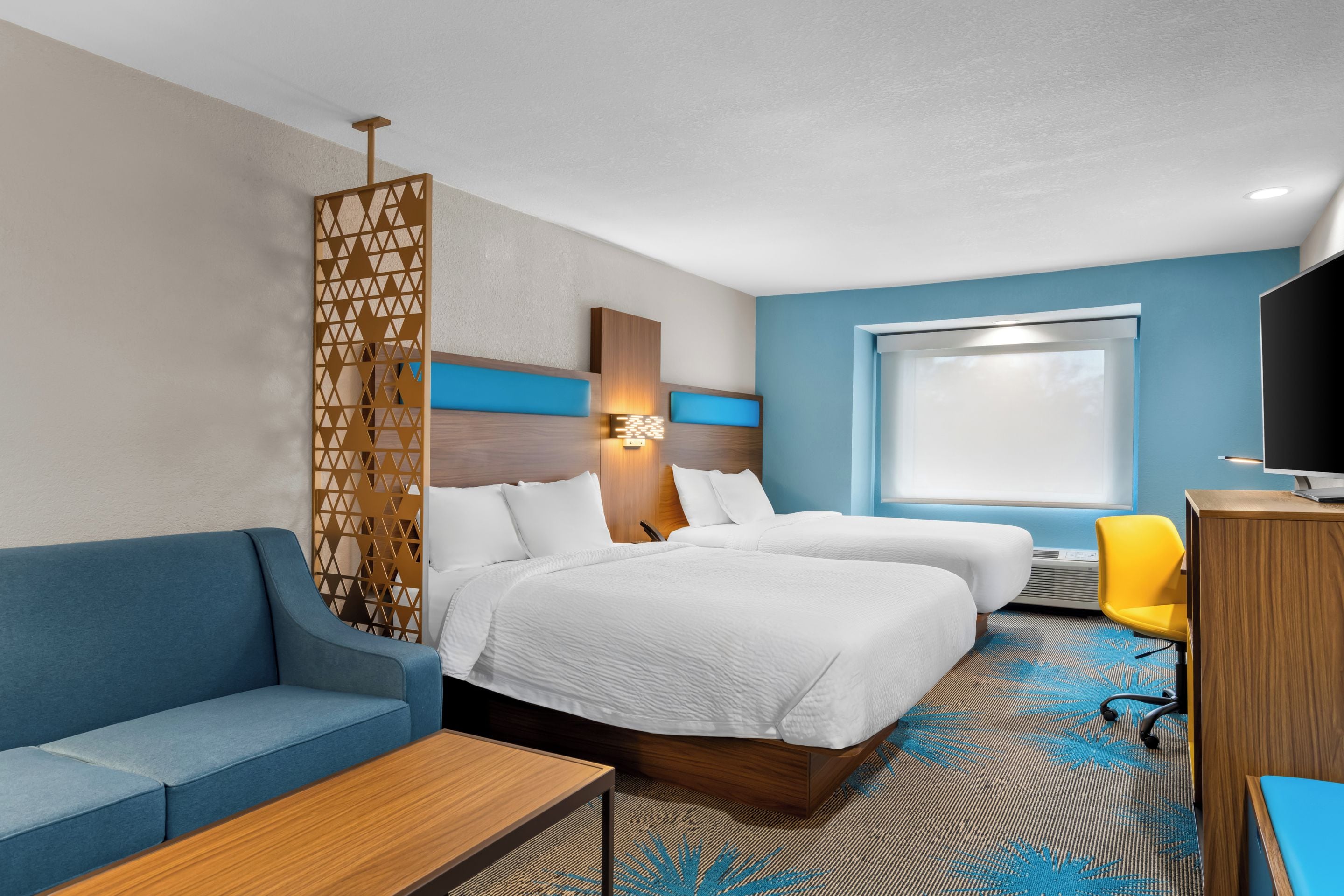 Una habitación de hotel con dos camas, un sofá, un escritorio, un televisor y una ventana.